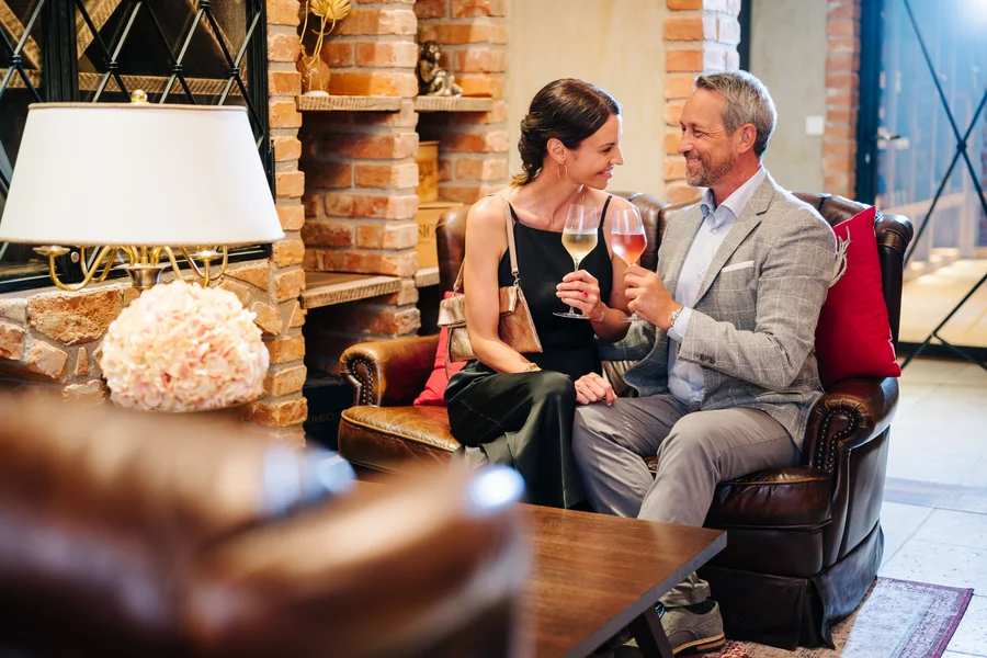 Paar stößt mit Wein an Ein elegant gekleidetes Paar sitzt auf einem Ledersofa und stößt mit zwei Gläsern Wein an.